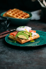 Belgian waffles with salmon, poached egg, avocado and cream cheese on a turquoise plate. Healthy breakfast at the table