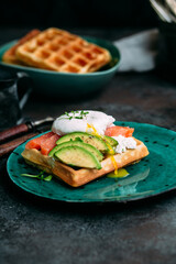 Belgian waffles with salmon, poached egg, avocado and cream cheese on a turquoise plate. Healthy breakfast at the table