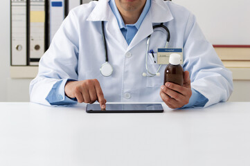 Photo of a young doctor consulting a tablet for a prescription in his office with a bottle of antipyretic syrup in hand