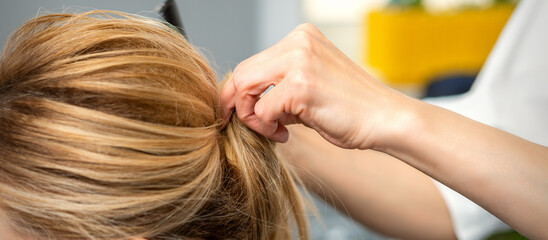 Naklejka premium Close up of female hairdresser styling blonde hair of a young woman in a beauty salon