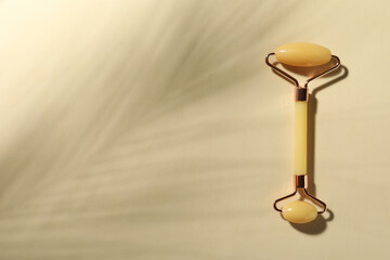 Natural jade face roller on beige background, top view. Space for text