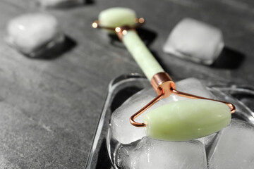 Natural jade face roller and ice cubes on grey background, closeup