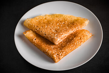 Thin pancakes on a plate on a black background, traditional Russian food.