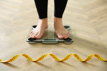 Woman with measuring tape standing on scales indoors, closeup. Overweight problem