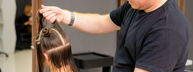 Male hairdresser holds and splits long hair of a young brunette woman in a hair salon