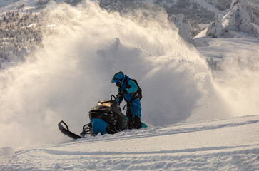 a guy on a mountain snowmobile skids and pushes full throttle, letting out large fountains of snow from under the tracks. bright skidoo motorbike and suit without brands. Winter fun. panoramic view