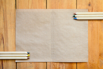Old sheet of paper with pencils on a wooden surface. Free white space on the sheet for text or sketch