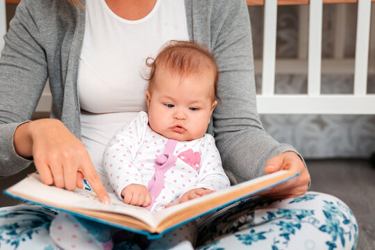 Mother shows pictures in a book for her baby. Close up portrait of baby. The concept of parenting