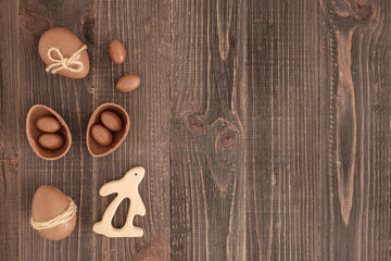 Flat lay of decorated chocolate eggs, candies and bunny on the wooden background. Easter decoration. Cope space, place for text. Eater gift.