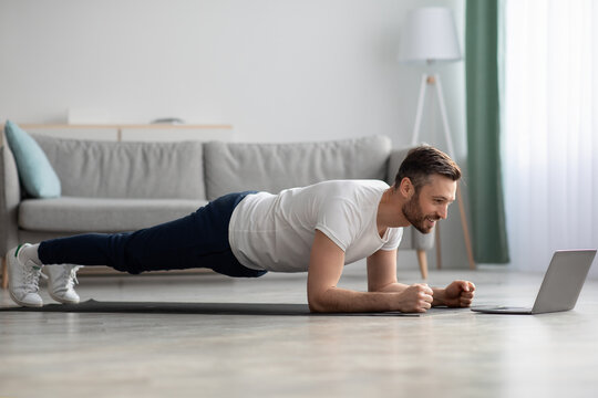 Middle-aged man in sportswear planking in front of laptop - Powered by Adobe
