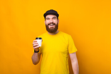 Joyful young bearded hipster man drinking cup of coffee on the go