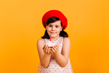 Blissful kid celebrating birthday. Front view of preteen girl with cake isolated on yellow background.