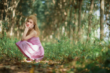 Lovely young lady wearing pink dress sit and rest in woods.