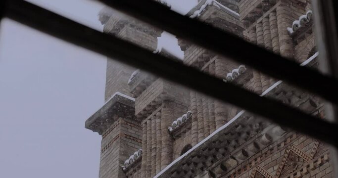 Snow outside the window and a beautiful brick building. Beautiful winter and falling snow. The glass distorted the picture a little, looking at the falling snow.