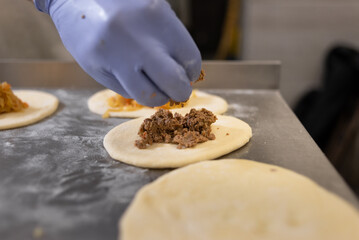 Put the filling on a small pie with the hands of the chef. Raw baked goods lie on a metal baking sheet in a bakery.
