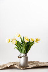 Fototapeta na wymiar gelb weiße Tulpen in einer Zink Milchkanne auf braunem Packpapier vor weißem Hintergrund arrangiert - minimalistisch, shabby chic, skandinavisch, rustikal, boho, modern, Tulpenstrauß, Blumendeko