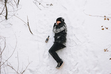 A drunken homeless man in a black coat lies sleeping on his side on white snow in a cold frosty...
