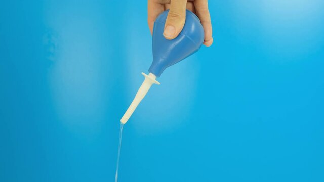 Hand with a blue enema puming, compressing, squeezing and injecting water on a blue background