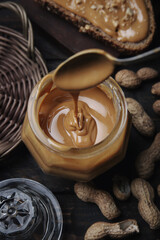 Organic Peanut Butter in Glass Jar with Peanuts in Shell on Wooden Background