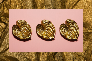 Modern stylish decor concept. Three golden anthurium flowers on pink background. Flat lay. Golden frame made of wrapping paper. Close up. Studio shot © Augustino