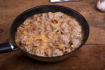 Chicken meatballs with cheese in a creamy sauce in a frying pan on a wooden kitchen table, top view, close-up - Swedish cuisine