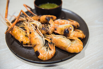 Grilled river shrimps with chili seafood sauce on black plate on wooden table.