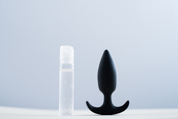BLACK ANAL PLUG AND A BOTTLE OF LUBRICANTS ON A TABLE ON A WHITE BACKGROUND.