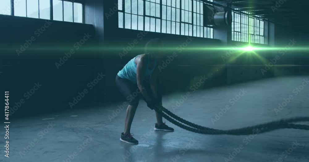 Poster animation of shining light floating over woman exercising with ropes in an abandoned building
