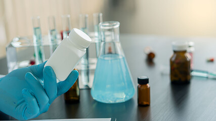 A medicine bottle in the hand of a doctor holding a doctor prescribing medicine to the patient the doctor sitting at the desk in the office with a vaccine trial bottle on the table