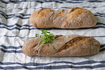 Two mini baguettes and microgreens on a crumpled striped canvas.
