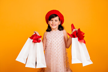 Wonderful kid in red beret posing with store bags. Cheerful child smiling after shopping.