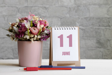 june 11. 11th day of the month, calendar date.A delicate bouquet of flowers in a pink vase, two pencils and a calendar with a date for the day on a wooden surface