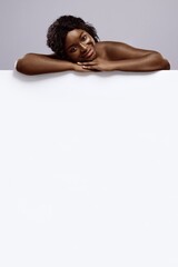 Beauty And Wellness. Attractive nude african woman leaning at white advertisement board