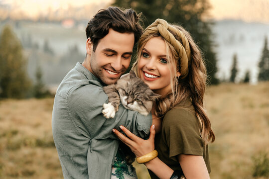 Beautiful sensual couple hug together with the cat and smile cheerfully in nature.