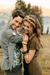 Beautiful sensual couple hug together with the cat and smile cheerfully in nature.