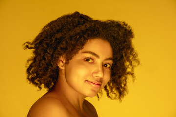 Dreams. Beautiful african-american woman's portrait isolated on yellow golden studio background in neon, monochrome. Concept of human emotions, facial expression, sales, ad, fashion and beauty.