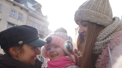 Obraz premium Lesbian couple tourists posing, taking selfie with adoption child girl kid on city street. Two women making photo or video chat with family and friends using smartphone during winter holidays vacation