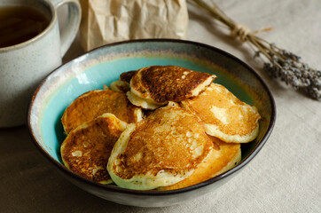 Fried kefir pancakes in a blue plate, lavender flowers and a mug with a drink.	