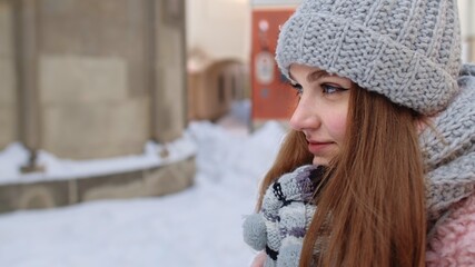 Close-up of young tourist woman warming her cold hands outdoors in winter day. Portrait of Caucasian traveler girl rubs her hands in gloves trying to keep warm in frosty weather on street in city