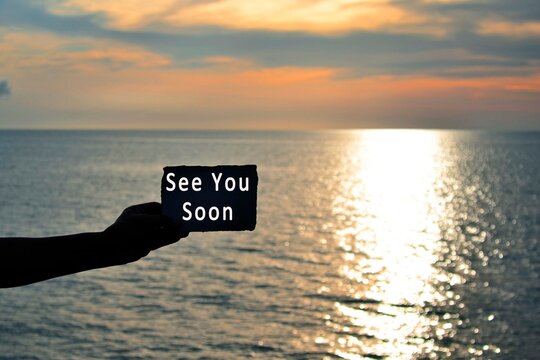 See you soon text on hand holding torn paper with blurred background of sunset at the beach of Tanjung Aru Beach, Kota Kinabalu, Borneo,Sabah, Malaysia