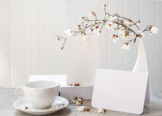 Mock up white  invitation cards ,coffee cup and beautiful Nodding Clerodendron flowers in modern vase set on concrete table with white wood background,greeting card in soft tone still life