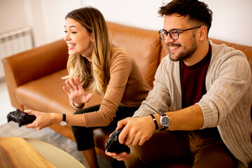 Young couple playing video games at home, sitting on sofa and enjoying themselves