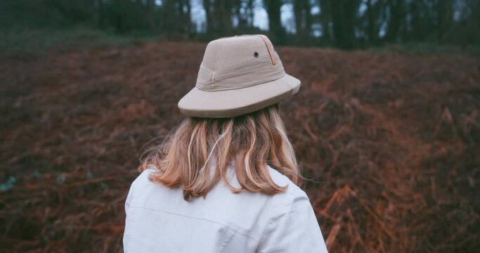 A young woman wearing a safari hat is walking in the wilderness