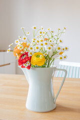 Bouquet of fresh Persian buttercup flowers and daisies in a mint green coffee pot from the 60ies on a wooden table . Interior design in Scandinavian style.