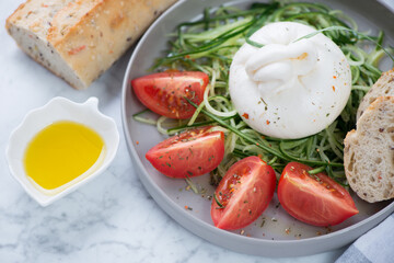 Closeup of salad with burrata cheese, cucumber and tomatoes served on a grey plate, horizontal shot, selective focus