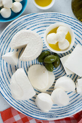 Mozzarella, ricotta and feta cheese with green olives and olive oil on a blue and white plate,...