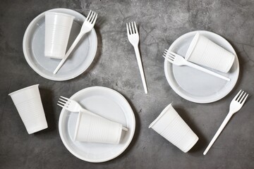 Plastic dishes, disposable tableware, plates, forks, glasses on a concrete grey background. Caring for the environment. The problem is recycling. Reuse. Place for text.