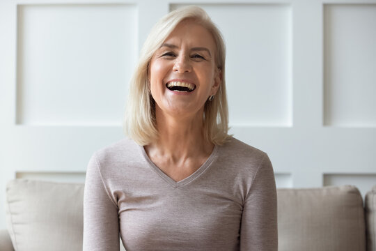 Vivacious Elderly 60s Blond Woman With Wide Toothy Candid Smile Sit On Sofa Look At Camera Head Shot Portrait, Having Video Call Lively Positive Conversation With Friend Via Online Application Concept
