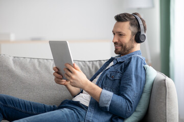 Joyful middle-aged man usind headset and digital tablet