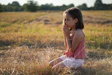 Little Girl closed her eyes, praying in a field. Hands folded in prayer.